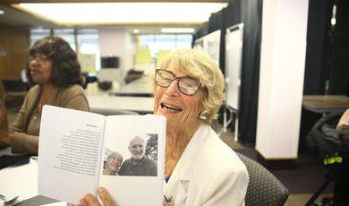 Frances Sharon smiles while holding up a book that contains a photo of her and a man 