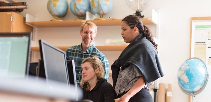 Professor Robert Hellstrom with 2 students at a computer in a classroom surrounded by globes.