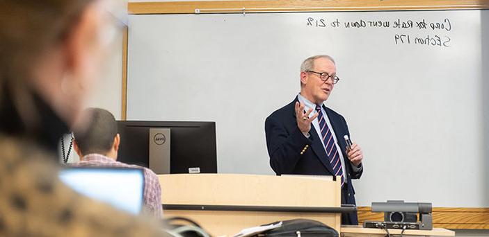 马克·克劳利教授在白板前讲课，白板上写着公司税率的笔记